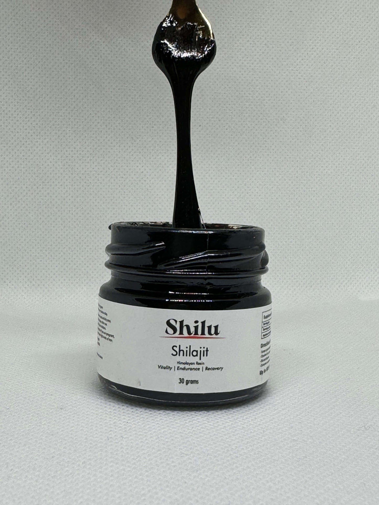Jar of Shilajit nz with a spoonful being poured over it on a gray background